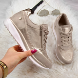 Scarpe da ginnastica beige con dettagli metallici, suola bianca, su tappeto peloso bianco. Occhiali da sole e orologio sullo sfondo.