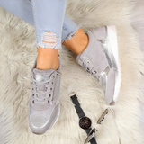 Scarpe da ginnastica grigie e argento su tappeto bianco, jeans strappati, orologio nero e occhiali da sole. Moda casual donna, stile trendy.