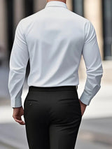 Uomo in camicia bianca e pantaloni neri, visto di spalle, cammina in ambiente urbano. Abbigliamento formale, moda maschile elegante.