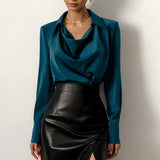 Camicia elegante in seta blu petrolio con colletto drappeggiato, abbinata a gonna nera in pelle a vita alta. Moda donna, abbigliamento chic.