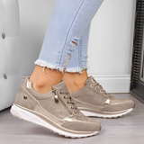 Scarpe da ginnastica beige metallizzate su pavimento in legno, indossate con jeans chiari strappati. Design moderno, casual e alla moda.