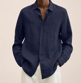 Camicia lino uomo blu scuro, maniche lunghe, abbottonata, stile casual elegante, indossata con pantaloni chiari. Moda maschile estiva.