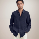 Giovane uomo in camicia di lino blu scuro, maniche lunghe, con pantaloni chiari. Moda maschile elegante, stile casual chic. Sfondo neutro.