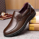 Scarpa da uomo in pelle marrone lucida, design elegante e suola robusta, posizionata su un tavolo con libri e accessori di lusso sullo sfondo.