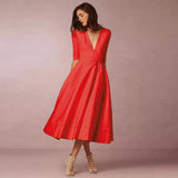 Donna con elegante abito rosso a maniche corte e scollo a V, lunghezza midi. Scarpe con tacco beige. Sfondo neutro. Moda femminile chic.