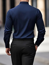 Uomo in camicia blu scuro e pantaloni neri, visto di spalle, cammina in città. Moda maschile elegante, abbigliamento formale, stile urbano.
