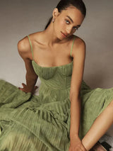 Modella in abito verde elegante, seduta su sfondo neutro. Vestito plissettato, spalline sottili, look sofisticato. Moda donna, abbigliamento chic.
