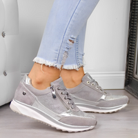 Scarpe da ginnastica grigie da donna con dettagli metallici, indossate con jeans chiari strappati. Design moderno e casual per look alla moda.