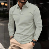 Uomo con camicia polo grigia e pantaloni beige, orologio nero al polso, posa casual in ambiente urbano. Moda maschile elegante e moderna.
