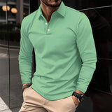 Uomo con camicia verde a maniche lunghe, pantaloni beige, orologio nero, in piedi su marciapiede urbano. Moda maschile casual elegante.