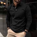 Uomo con camicia nera a maniche lunghe e pantaloni beige, orologio al polso, in piedi davanti a un edificio moderno. Moda maschile elegante.