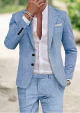 Uomo in abito elegante azzurro, camicia bianca aperta, orologio e bracciale argento, sfondo sfocato. Moda maschile, stile estivo.