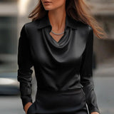Donna con camicia di seta nera elegante, collana d'argento, sfondo urbano sfocato. Moda femminile, abbigliamento di lusso, stile sofisticato.