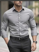Uomo in camicia grigia elegante, maniche lunghe, abbinata a pantaloni neri. Moda maschile, abbigliamento formale, stile moderno.