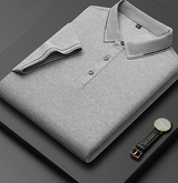 Camicia polo grigia piegata su sfondo nero, con orologio elegante accanto. Moda uomo, abbigliamento casual, stile minimalista.