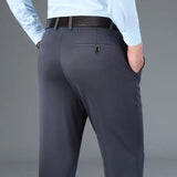 Pantaloni eleganti da uomo in tessuto grigio scuro, tasche posteriori con bottone, camicia azzurra, cintura in pelle nera. Moda maschile formale.